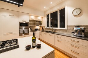 A modern kitchen with a gas stove, wine glasses, a bottle of wine, a coffee machine, and a clock on the wall. - Bel Air Mansion | 6BR | Sleeps 12 | Near CBD (Christchurch)