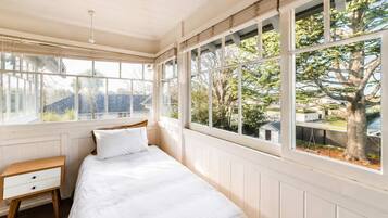 A bedroom with a bed, a bedside table, and large windows offering a view of the outdoors.