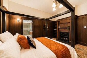 A bedroom with a bed, a fireplace, and a view into a bathroom.