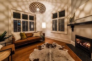 A living room with a leather sofa, a cowhide rug, a fireplace, and a hanging light fixture. - Bel Air Mansion | 6BR | Sleeps 12 | Near CBD (Christchurch)