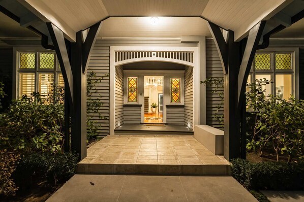 A house entrance with a covered porch, a staircase leading to the main door, and a small garden area with shrubs.