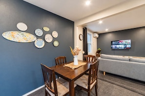 A dining area with a table, chairs, and a wall-mounted TV. - Richmond Cottage | 3BR + Hot Tub | Parking (Christchurch)