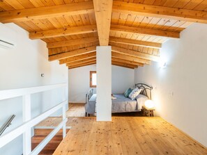 Un dormitorio con techo de madera inclinado, una cama con almohadas, una mesita de noche con lámpara y una ventana.