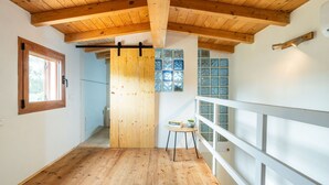 Une pièce avec un plancher en bois, un plafond en bois, une fenêtre avec un cadre en bois et une rambarde blanche.