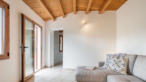 Un vaste espace de vie doté d’un canapé gris, d’un plafond en bois et d’une porte-fenêtre coulissante donnant sur un couloir.