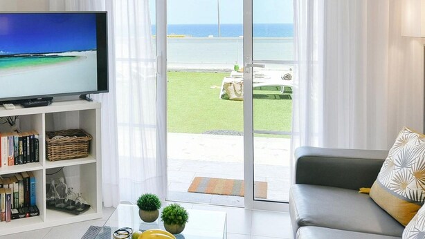 Una sala de estar con televisor, estanterías, una mesa de centro con objetos decorativos y un sofá con cojines estampados.