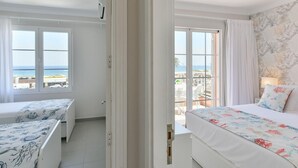 Habitación de hotel con balcón, cama con colcha estampada, escritorio con mantel decorado y vista al mar.