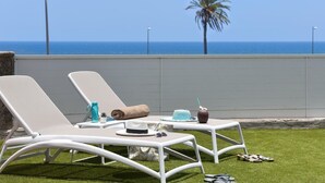 Dos sillones blancos en una zona ajardinada con vistas al océano y una palmera.