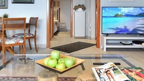 A living room with a glass coffee table, a bowl of green apples, a magazine, and a television displaying a beach scene. - Wonderful private villa for 6 people with private pool and TV (Arucas)