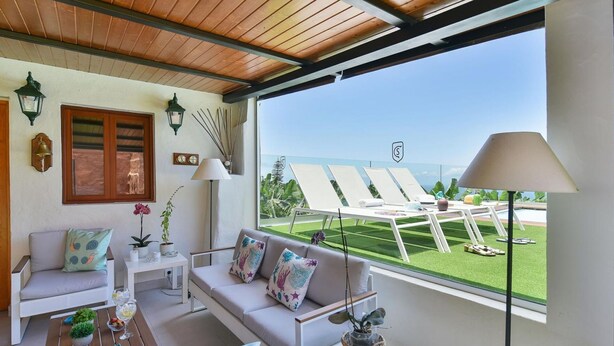 A sunlit room with a view of a pool and lounge chairs, featuring a sofa, a coffee table, and a lamp. - Wonderful private villa for 6 people with private pool and TV (Arucas)