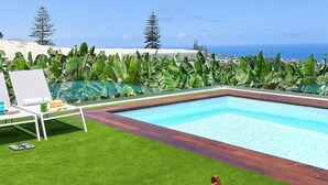 A swimming pool with a wooden deck, surrounded by lush green grass and banana plants. - Wonderful private villa for 6 people with private pool and TV (Arucas)