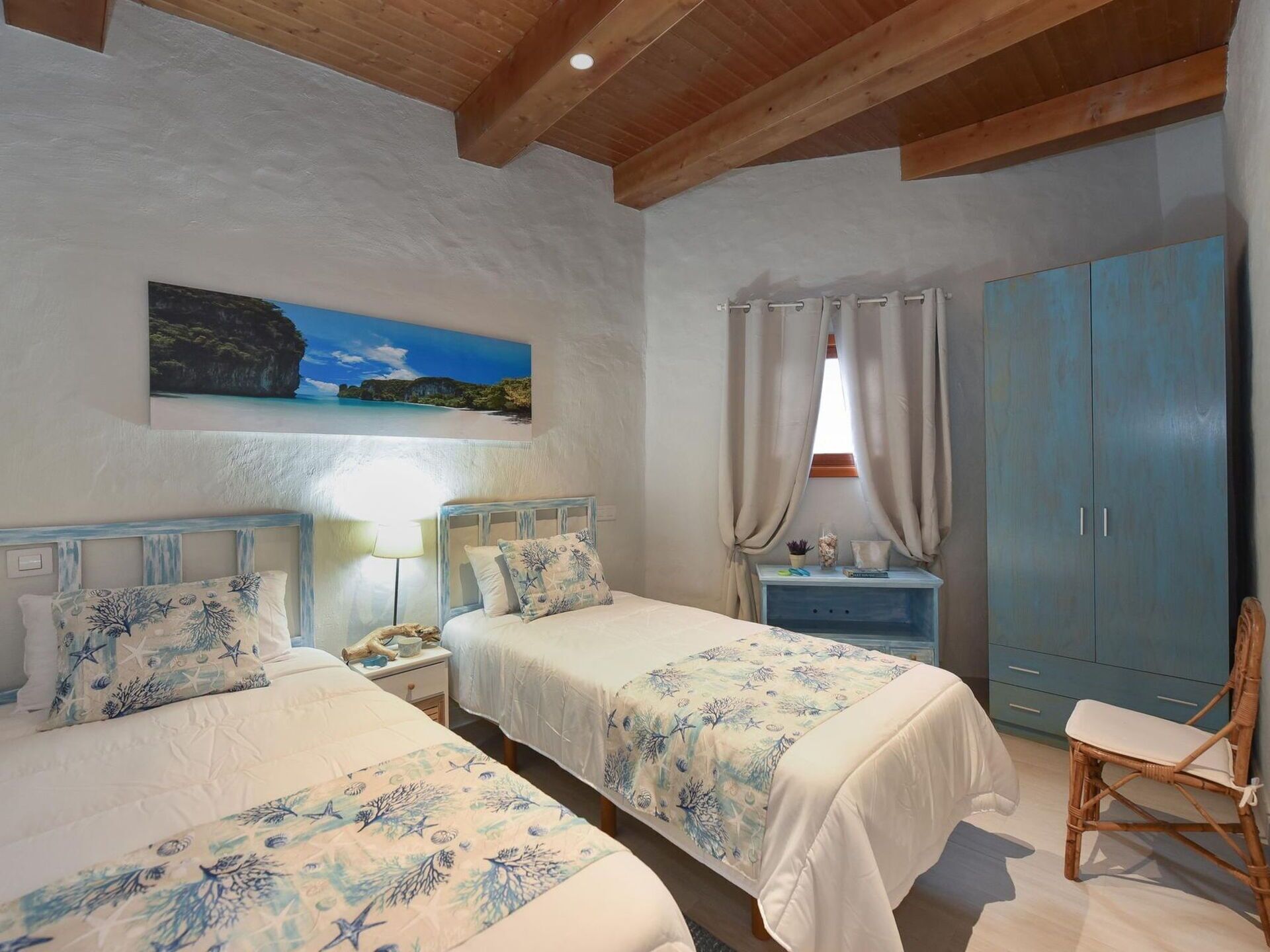 Un dormitorio con dos camas, una mesita de noche, una silla, un armario y un cuadro de una playa.