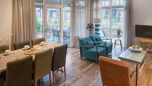 A modern living room with a dining area, large windows, and a TV.