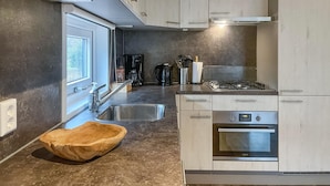 A modern kitchen with a built-in oven, a stainless steel sink, and a wooden bowl on the counter.