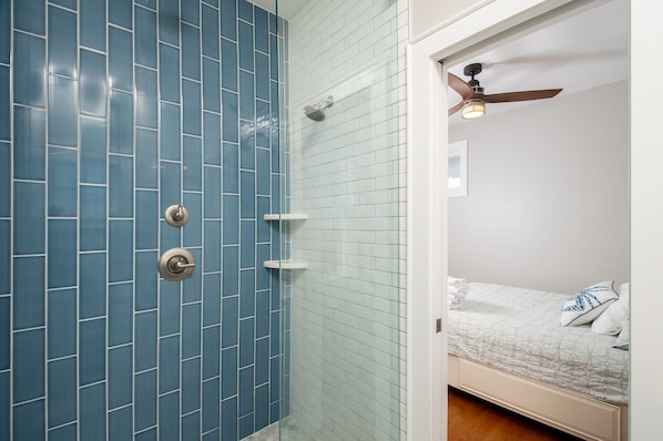 A bathroom with blue tiled walls, a shower, and a bed with a white and blue patterned bedspread.