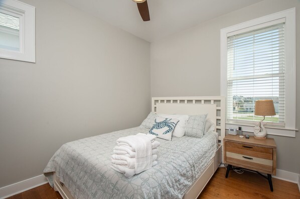 A bedroom with a bed, a bedside table with a lamp, and a window with blinds. - Reef Points Wardroom in Atlantic Beach, NC (Atlantic Beach)