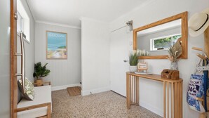 A hallway with a wooden console table, a framed picture, a mirror, and a hat on the wall. - TreasureView Beach - Three bedroom option #9a (Coolum Beach)
