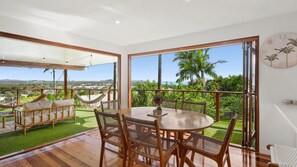 A spacious balcony with a view of the sea, a wooden dining table, wicker chairs, and a hammock.