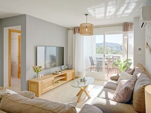 Relax in this stylish living room with a large flat-screen TV, comfortable sofa, and sliding glass door leading to an outdoor patio.