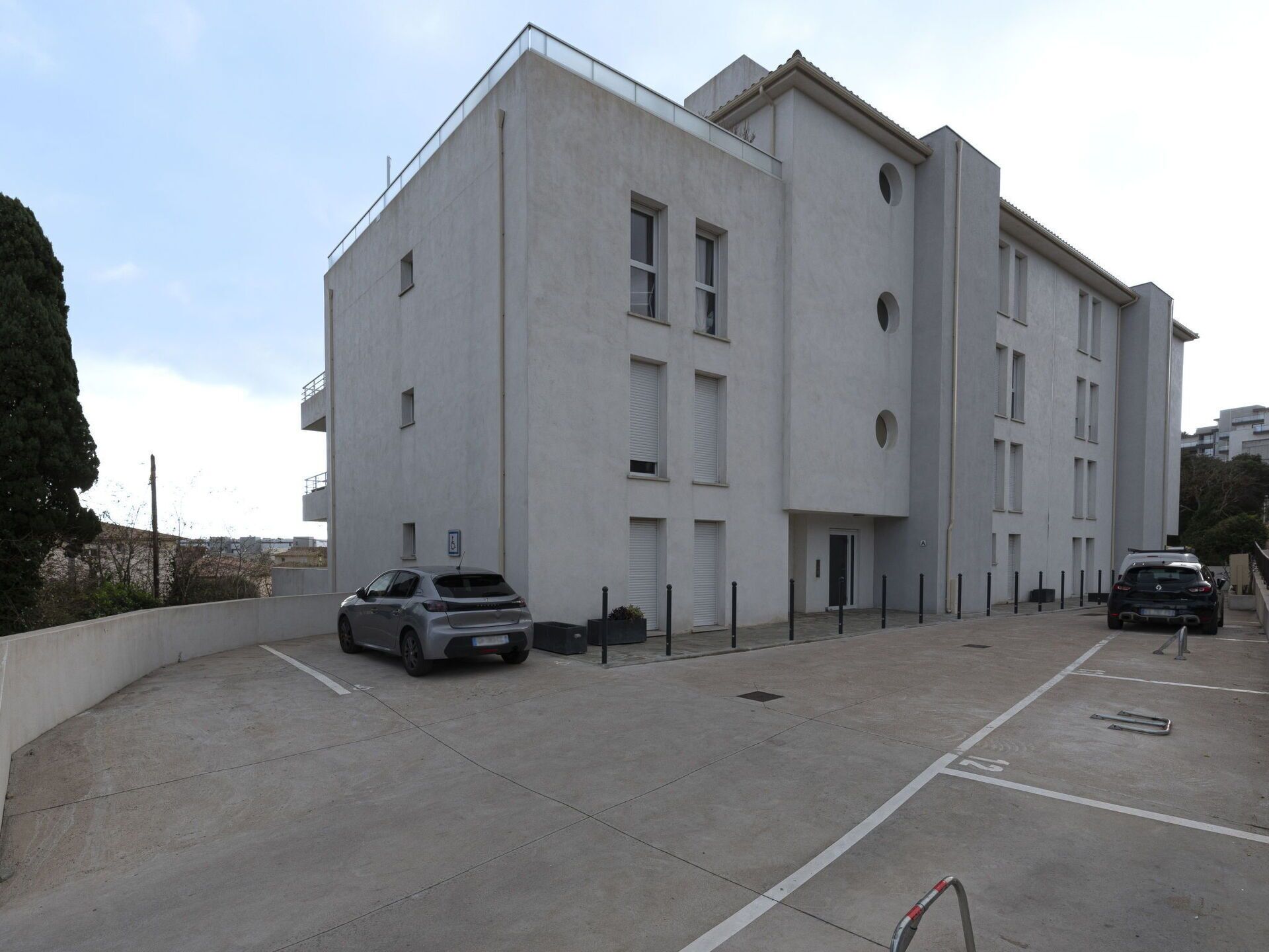 Un edificio moderno con fachada plana, múltiples ventanas y un estacionamiento con dos coches.