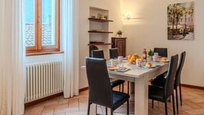 A dining area with a table set for four, chairs, a radiator, a window with curtains, and a wall-mounted shelf with decorative items. - Wonderful private villa for 6 guests with WIFI, TV, terrace and pets allowed (San Mamete)