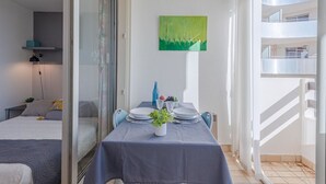 A balcony with a dining table set for two, a potted plant, and a green painting on the wall. - Cosy apartment for 2 guests with WIFI, TV and balcony (Port Leucate)