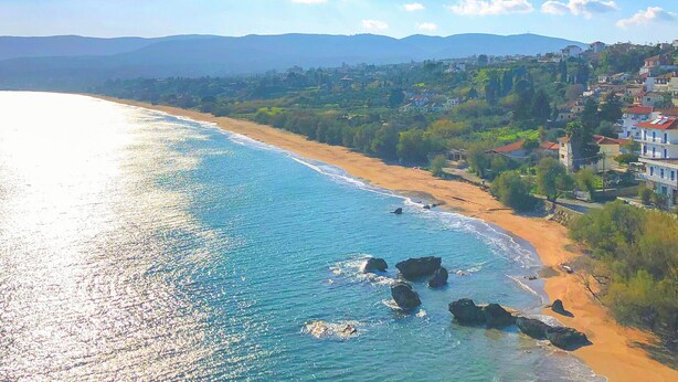 Vista costera con playa, costa rocosa y edificios en una ladera.
