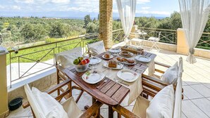 Un área de comedor al aire libre con una mesa dispuesta para cuatro personas, rodeada de sillas, con vistas a un paisaje pintoresco.