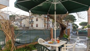 En udendørs patio med et bord, stole, en grøn parasol og et hegn i baggrunden.