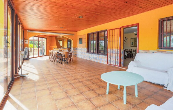 Een ruim terras met houten plafond, betegelde vloer en een eethoek met stoelen en tafel.