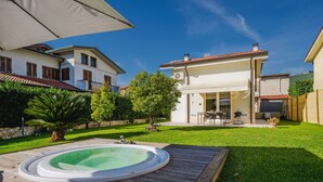 A two-story house with a backyard containing a wooden deck, a hot tub, and a well-maintained lawn.
