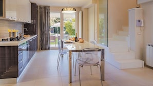A modern kitchen with a central island, a dining area with a glass table, and a staircase leading to an upper level.