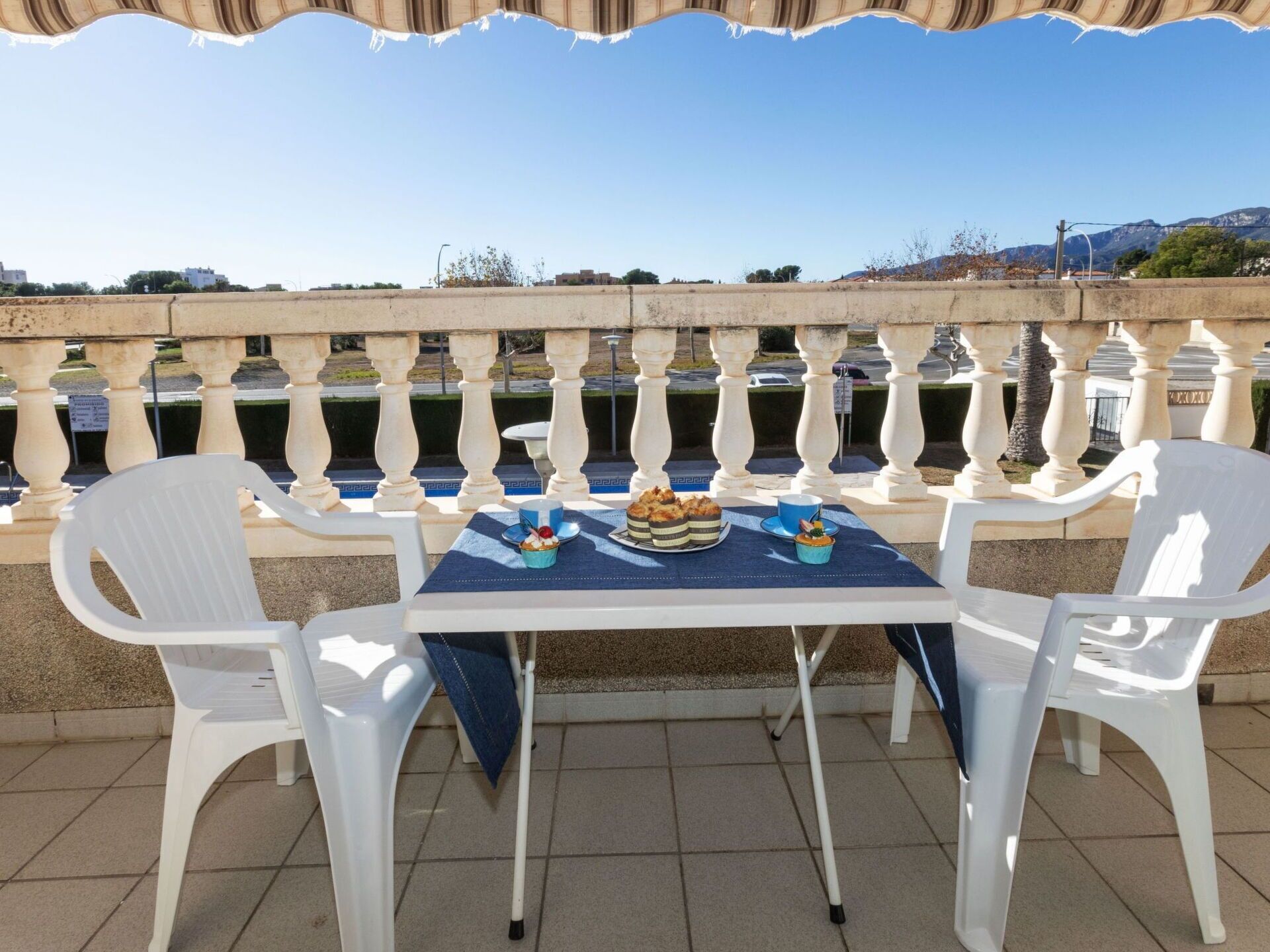 A table with chairs on an outdoor terrace with a view of the sea and mountains.