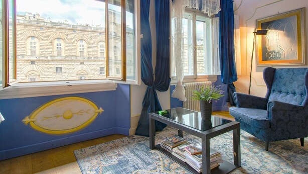 Ein Zimmer mit einem großen Fenster, einem blauen Sessel, einem Glastisch mit Zeitschriften und einer Heizung.