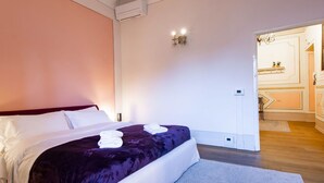 Ein Hotelzimmer mit Bett, einem durchgegangenen Tür erkennbaren Badezimmer und einem kleinen Tisch mit Lampe.