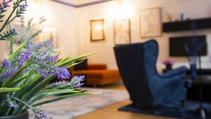 Ein Wohnzimmer mit einem dunkelblauen Sessel, einem Blumentopf mit violetten Blüten und einem Holzboden.