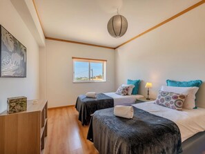 Un dormitorio con dos camas, una ventana, una lámpara colgante y suelo de madera.