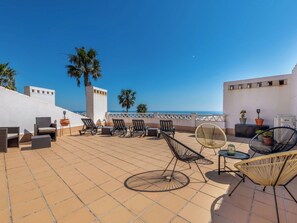 A rooftop terrace with outdoor seating, a view of the sea, and palm trees.