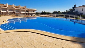 A swimming pool with a tiled deck, surrounded by buildings with balconies and a clear blue sky.