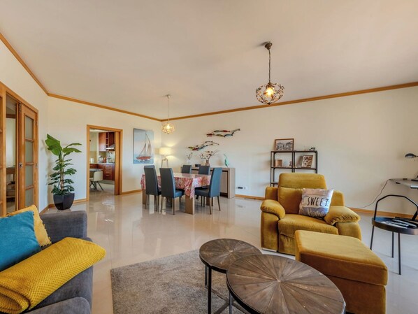 A modern living room with a dining area, a yellow armchair, a grey sofa, and a coffee table.