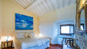 Un dormitorio con cama, un cuadro, una ventana, un espejo y una pared de piedra.