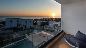 Un balcón con barandilla de vidrio que da a una vista panorámica de la ciudad al atardecer.