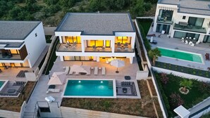 Una casa moderna de dos pisos con piscina, mobiliario exterior y un jardín cuidado.