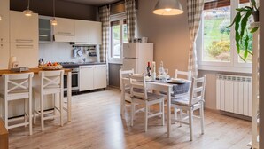 Une cuisine moderne avec des meubles blancs, un coin repas avec des chaises blanches et une grande fenêtre agrémentée de rideaux.