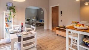 Un coin repas avec une table en bois dressée pour quatre personnes, une chaise blanche et une bibliothèque contenant des livres et une plante en pot.