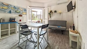 Een ruimtelijk ingerichte leefruimte met een eethoek, een bank en een aan de muur bevestigde televisie.