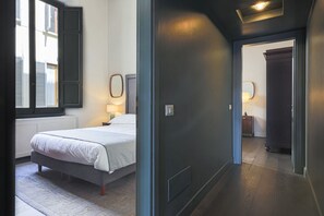 A bedroom with a bed, bedside lamps, a window with shutters, and a door leading to another room. - Apartments Florence - Palazzo Benci with river view · Palazzo Benci with river v (Firenze)