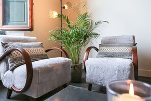Deux fauteuils rembourrés avec des accoudoirs en osier, une plante en pot et une bougie allumée sur une table.