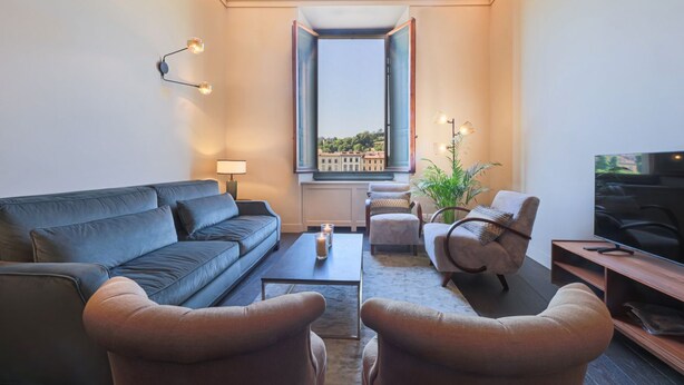 Una sala moderna con un sofá, sillones, una mesa de centro, un televisor y una ventana con vistas a edificios.