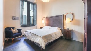 Un dormitorio con cama, una silla, una ventana, una mesita de noche y una lámpara.
